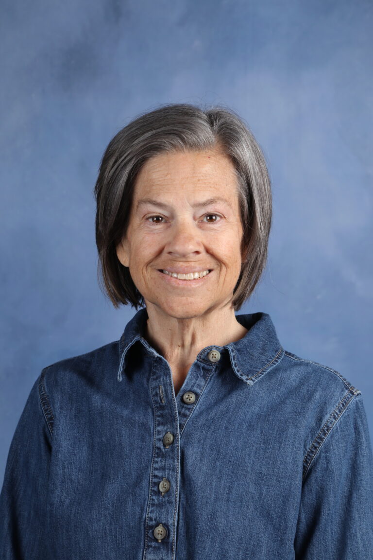 Portrait of Becky Holmes, smiling woman with gray hair wearing a denim shirt.