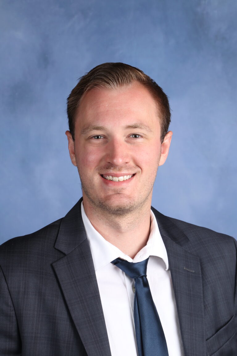 Professional headshot of a smiling man wearing a suit and tie.