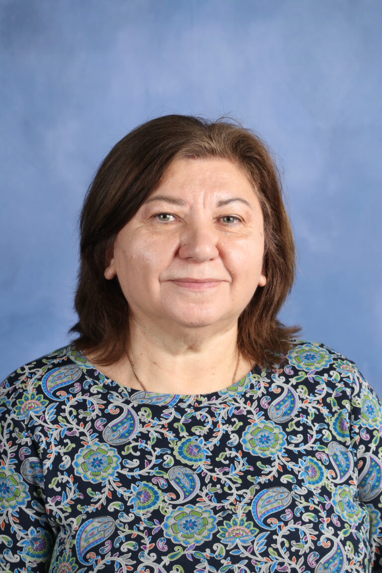 Tetyana Horoian, a woman with short brown hair, wearing a patterned blouse, smiles against a blue background.