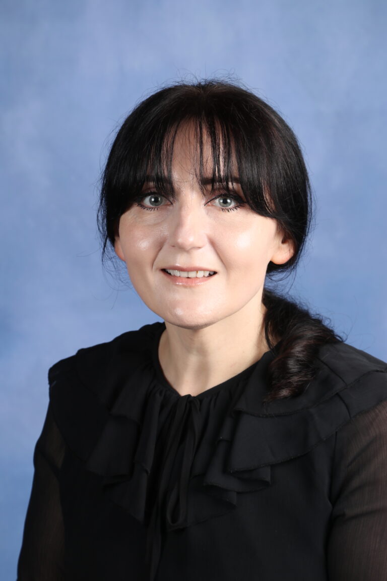 Tetyana Horoian portrait with dark hair and a black ruffled top against a blue background.