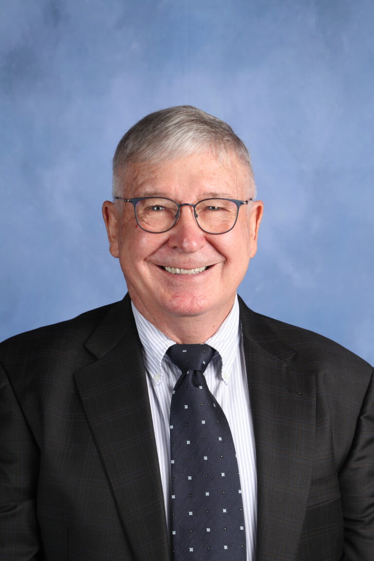 James Randolph Lewis, smiling in a suit and tie against a blue background.