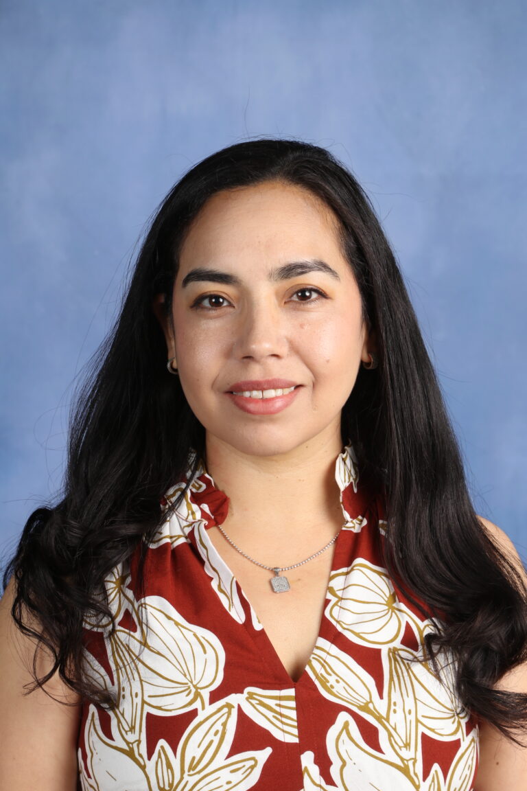 Perla Velazquez-Garcia, smiling with long dark hair and a floral top, against a blue background.