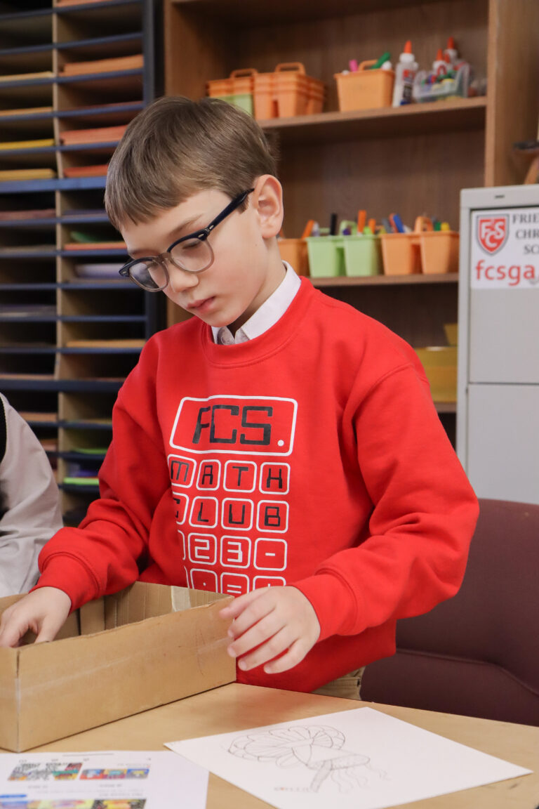Friendship Christian School student with Math Club sweatshirt looking in box.