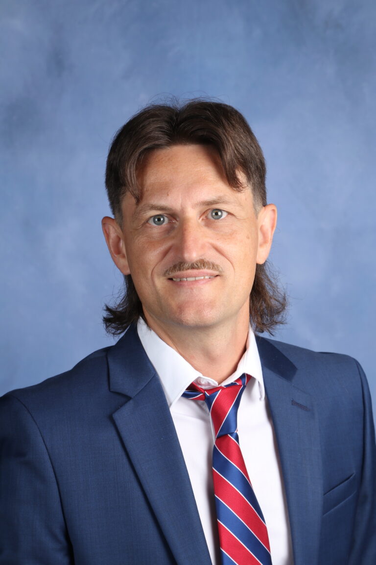 Anton Kraft portrait. Man in blue suit with red and blue striped tie smiles at the camera.