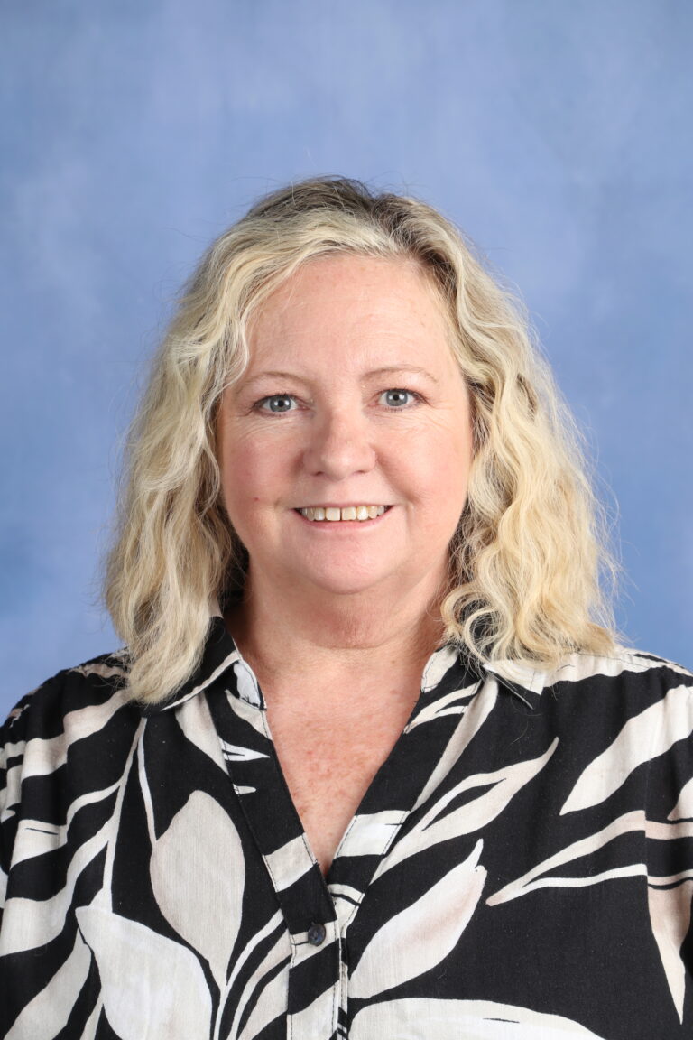Bettina Worley headshot, smiling with blonde curly hair against a blue background.