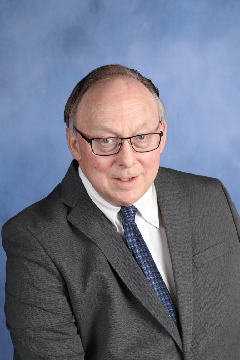 Dusty Dobbs in a suit, smiling for a professional headshot against a blue background.
