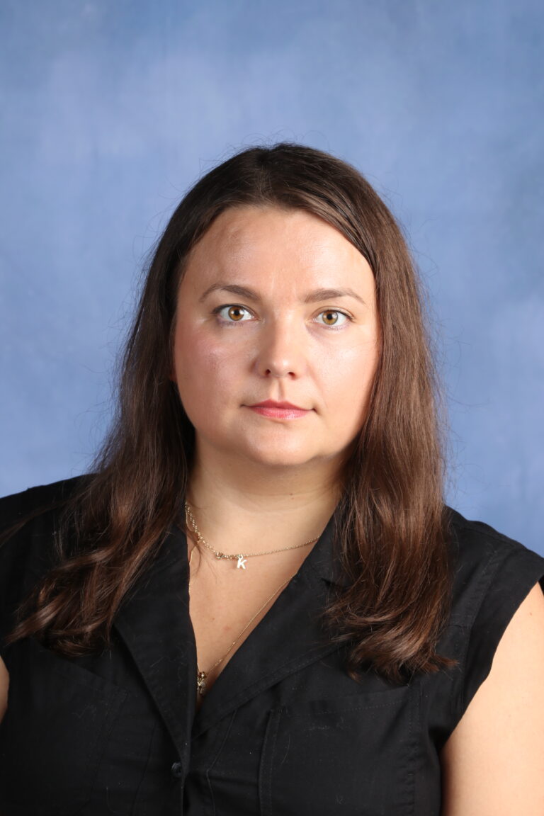 Ekaterina Danilova portrait. Woman with brown hair wearing a black shirt and gold necklace.