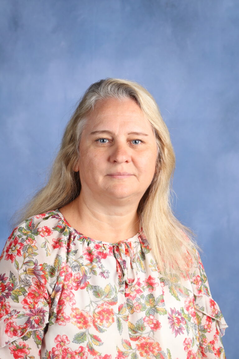 Portrait of Galina Rubets with long blonde hair wearing a floral blouse against a blue background.