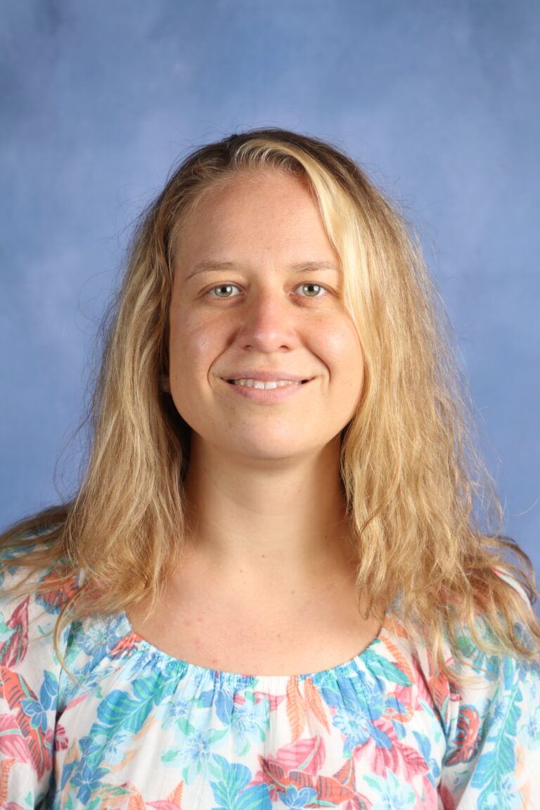 Helena Kirpich, headshot of a woman with blonde hair smiling against a blue background.