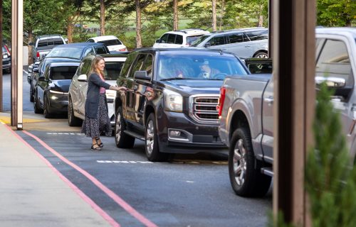 Cars line up at Friendship Christian School; a woman greets drivers.