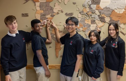 Students at Friendship Christian School point to locations on a world map, showcasing global learning and friendship.